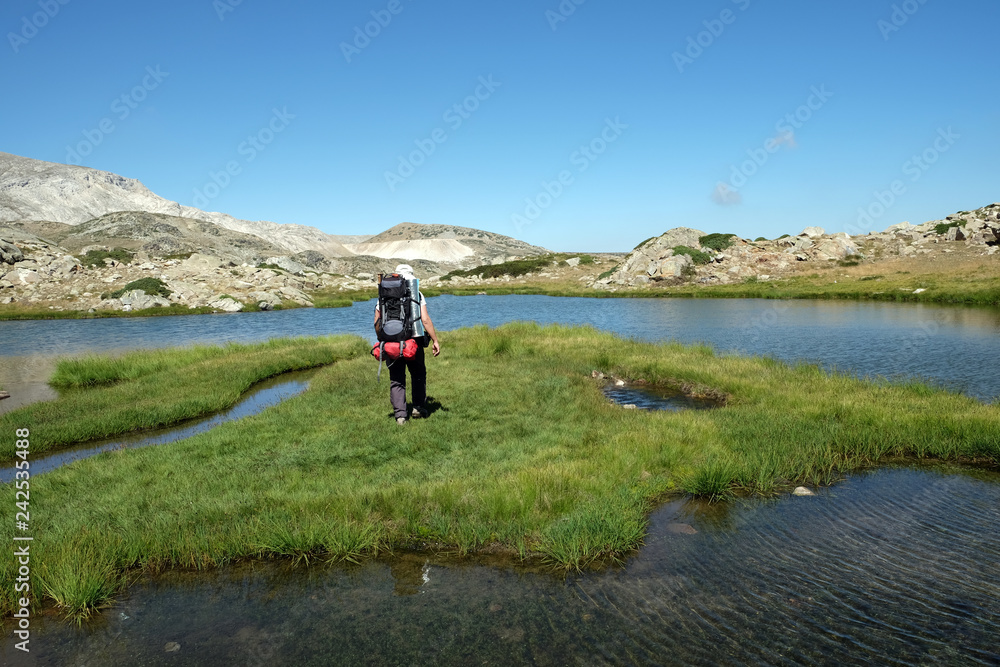 A hiker is walking on grassy island in glacial lake