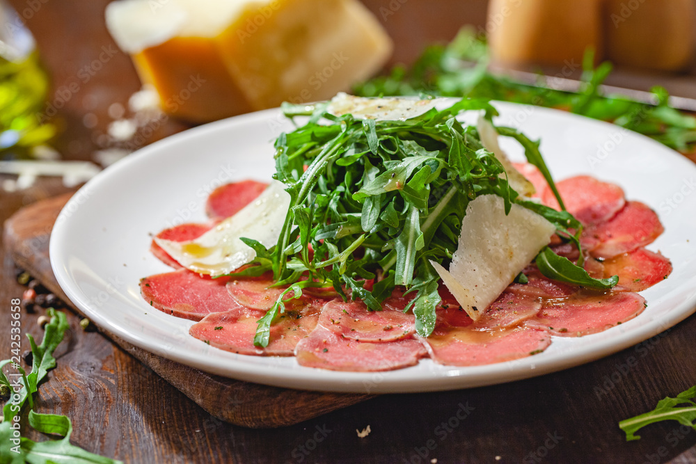 Meat carpaccio with arugula and parmesan cheese on white plate. Close up Meat carpaccio with arugula and parmesan cheese on white plate. Close up