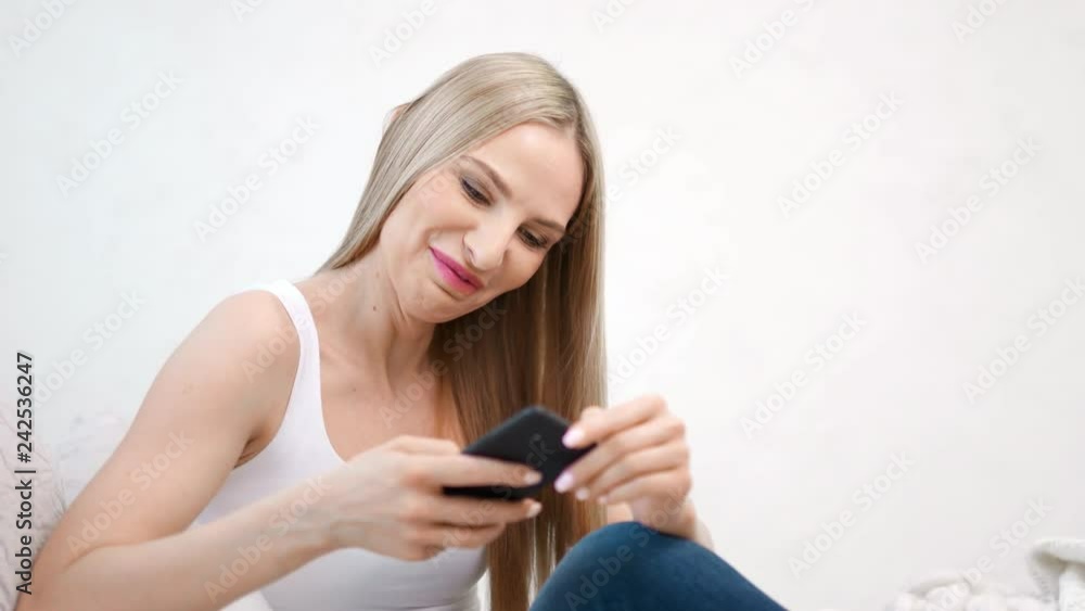 Enthusiastic smiling woman having good time chatting using smartphone at white studio background
