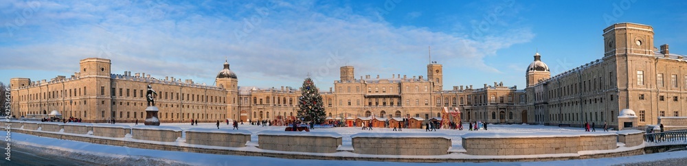 Fototapeta premium New Year and Christmas Fair on the parade ground. Panorama of the Palace Square with a monument to Paul 1, a Christmas tree, trade shops and slides for riding. Gatchina, Russia