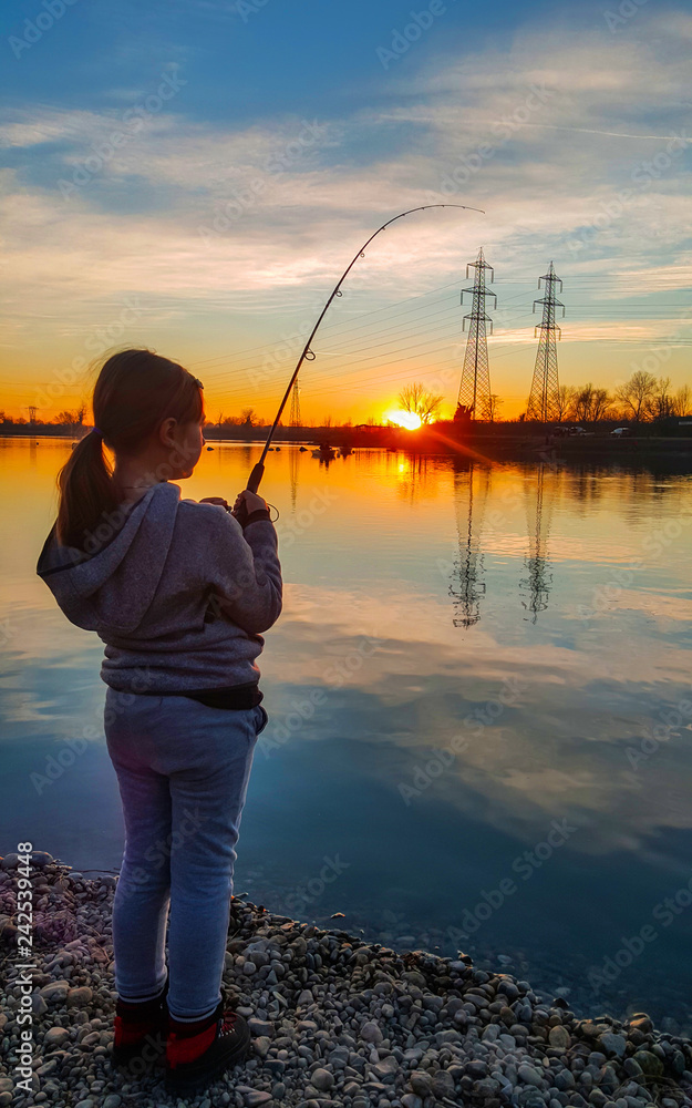 young girl fishing in a pond at sunset Stock Photo