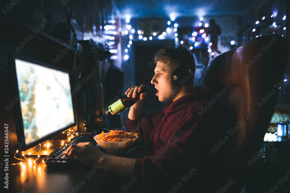 Portrait of a young man playing video games on a computer at home and  drinking beer,