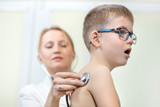Chłopiec podczas badania stetoskopem przez lekarza pediatrę głęboko oddycha przez otwarte usta.