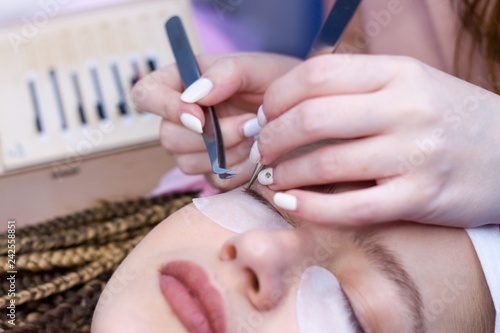 Eyelash Extension Procedure. Woman Eye with Long false Eyelashes. Close up macro shot of twezers in hands of beautican. photo