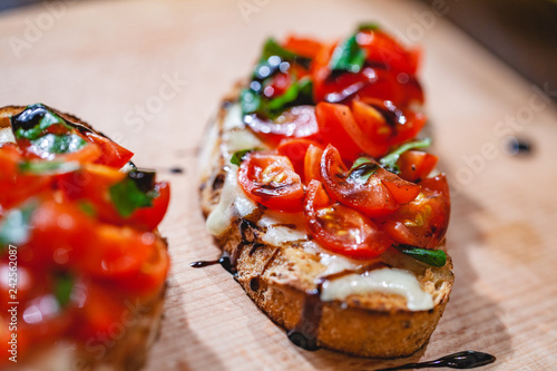 Traditional Italian bruschetta with cherry tomatoes, cheese, basil and balsamic vinegar on wooden board. Close up photo