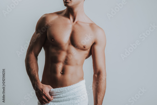 Muscular man having white towel on his hips and standing alone