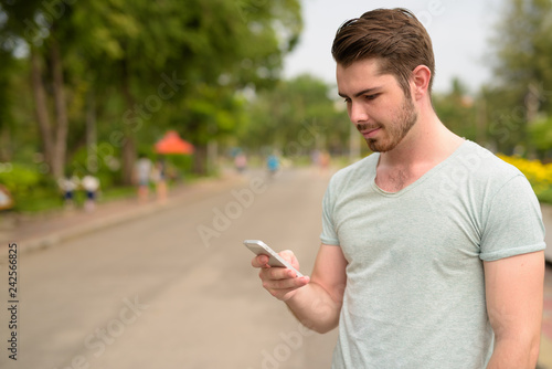 Portrait of young handsome man using mobile phone in park