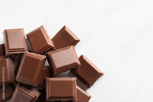 Pieces of tasty milk chocolate on white background, top view. Space for text