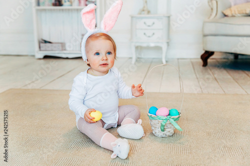 Little child girl wearing bunny ears on Easter day. Girl holding basket with painted eggs sitting on floor at home, having fun on Easter egg hunt. Happy Easter holiday celebration spring concept