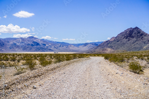 Travelling on an unpaved road through a remote area of Death Valley National Park; Racetrack Playa, mountains and blue sky in the background; California