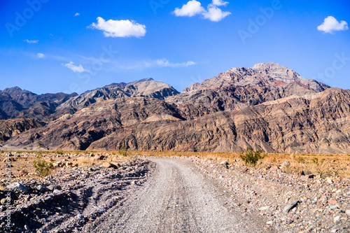 Driving on an unpaved road towards the entrance to Titus Canyon, Death Valley National Park; steep mountains in the background; California