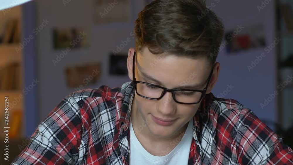 Handsome student smiling at camera, doing exercise at table, homeschooling Handsome student smiling at camera, doing exercise at table, homeschooling