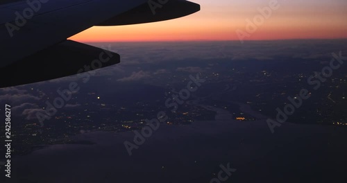 View from the airplane window of the moving cloudscape at sunset with the orange skyline, plane wing traveling above the cloud, 4k photo