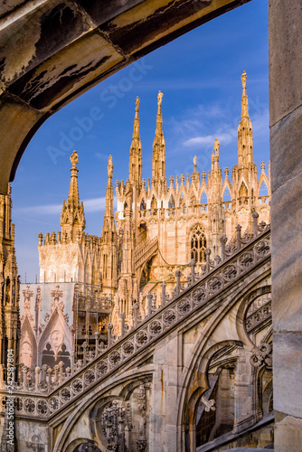 Vertical: Sunset exterior rooftop view fo Duomo di Milano with spires, blue sky, and architectural details