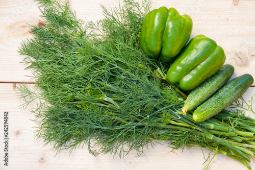 Fresh cucumbers, green peppers and dill on a wooden table.