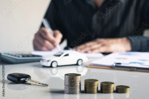 Businessman are saint documents about cars with some coins calculator and car toy on desk.