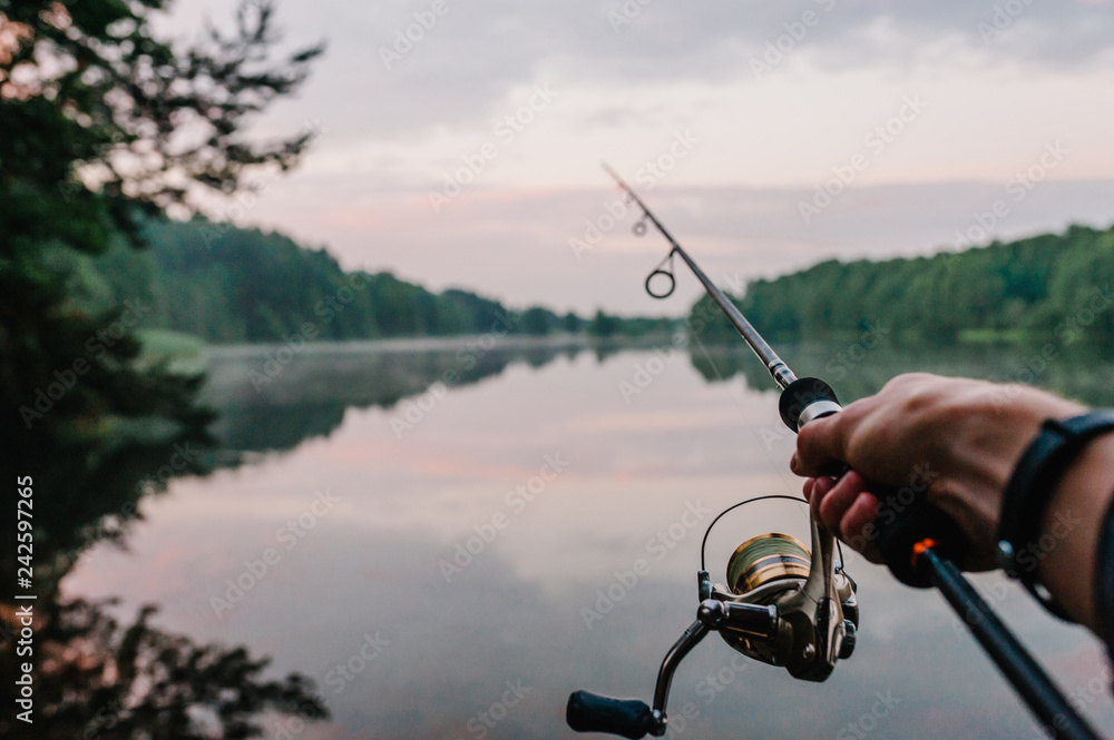 Fisherman with fishing rod, spinning reel on the background river bank.  Sunrise. Fog against the backdrop of lake. Misty morning. wild nature. The  concept of rural getaway. Article about fishing day. Stock