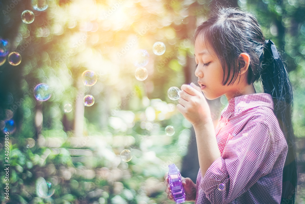 Asian girl wearing a pink shirt, being within the Park. She is currently blowing soap bubbles with fun. In the midst of the evening sun, concept of fun and freedom with copy space. Asian girl wearing a pink shirt, being within the Park. She is currently blowing soap bubbles with fun. In the midst of the evening sun, concept of fun and freedom with copy space.