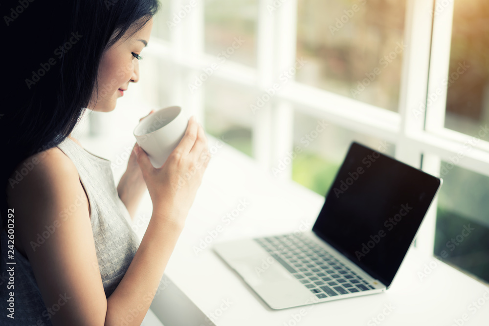 Asian beautiful young smiling woman working on laptop and drinking coffee while sitting in cafe or coffee shop. Asian beautiful young smiling woman working on laptop and drinking coffee while sitting in cafe or coffee shop.