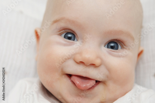 Cute five-month baby with blue eyes lies and smiles, shows tongue. Maternal care. Childcare. Close.