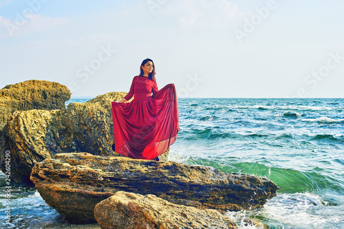 a young girl on the sea coast, a girl in a red dress resting sitting on the rocks