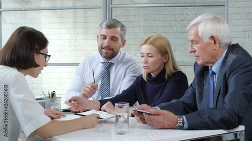 Tracking shot of businessmen and businesswoman giving skills assessment test to young female candidate in glasses during panel job interview