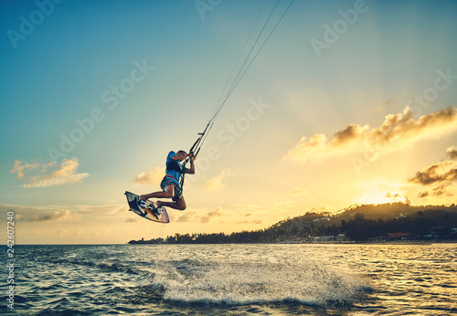 Young man kite boarder jumps over the sea at sunset           