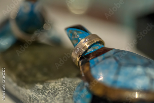 Two blue cheramic turtles on round stone decoration holding wedding rings.