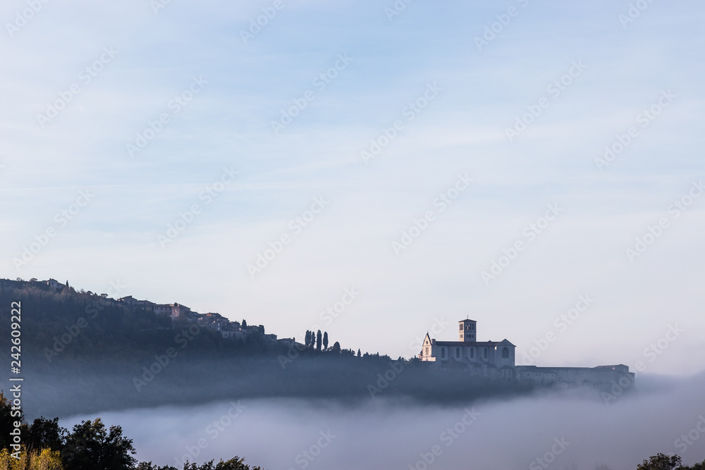 A view of St.Francis church in Assisi in the middle of mist beneath a blue sky with clouds