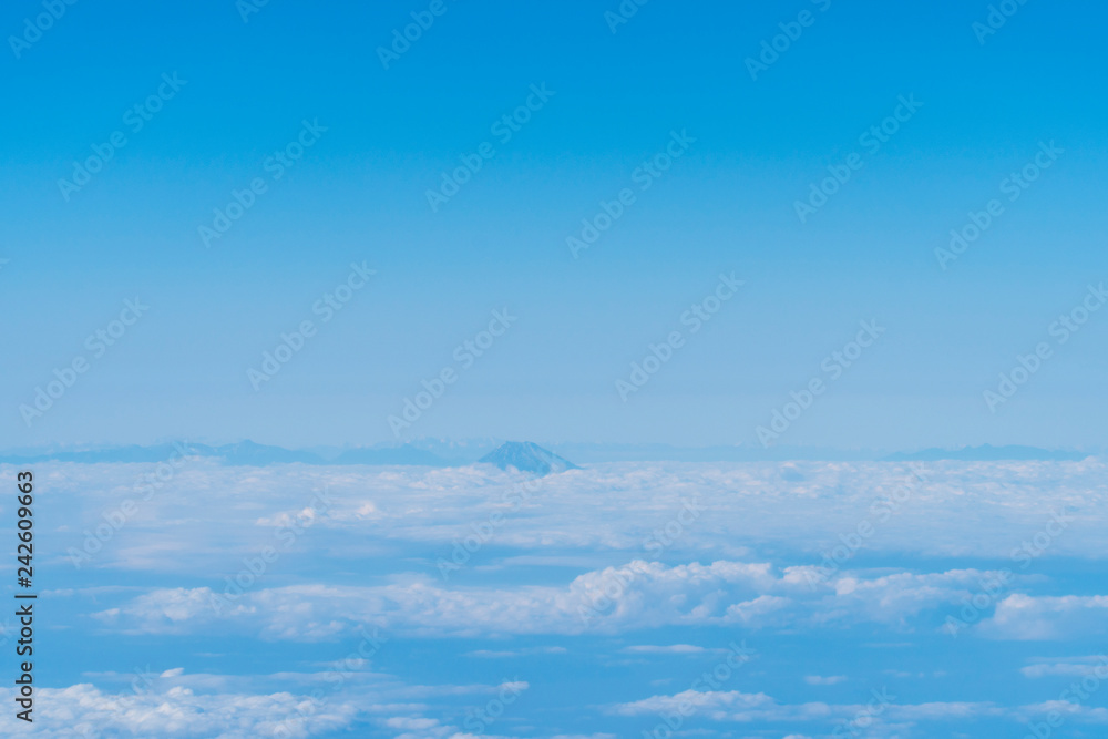 Fuji mountain top; appears at the horizon among the sea of clouds, blue sky; says hello through the airplane window on the way approaching Japan.
