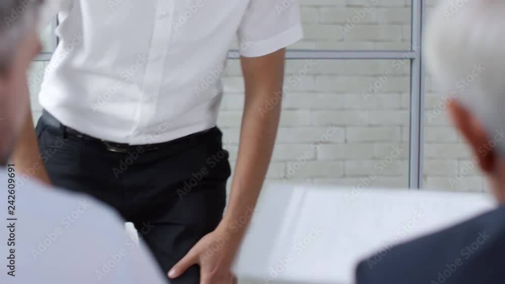 Handheld medium shot of young Arab man in glasses handing his CV to elderly businessman and bearded manager conducting job interview. He is sitting down and introducing himself Handheld medium shot of young Arab man in glasses handing his CV to elderly businessman and bearded manager conducting job interview. He is sitting down and introducing himself