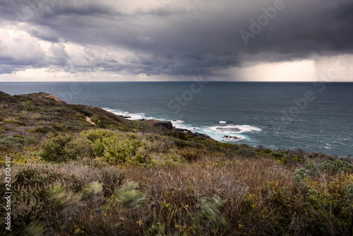 Long exposure shot of oceanside meadow and ocean shore with downpouring storm at London Bridge lookout in Portsea, Australia