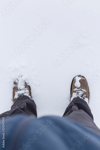 Low section of a person wearing outdoor clothes and shoes and standing on snow in the winter. Copy space.