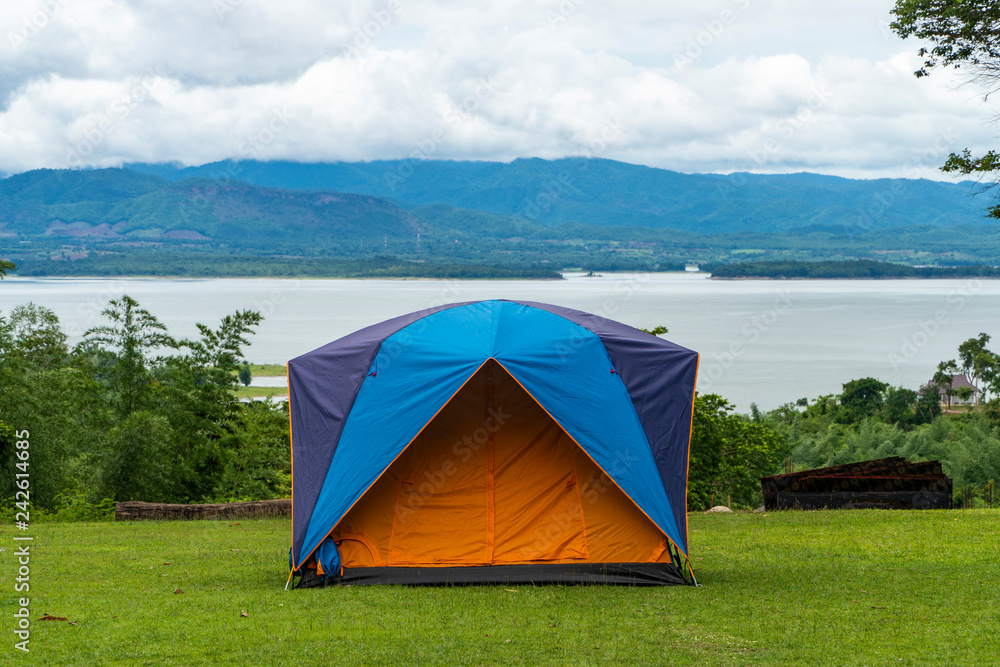 Tent camping located at a campsite on a hill of a national park in Thailand. The place looks into the river and the blue mountainous range background and cloudy sky.