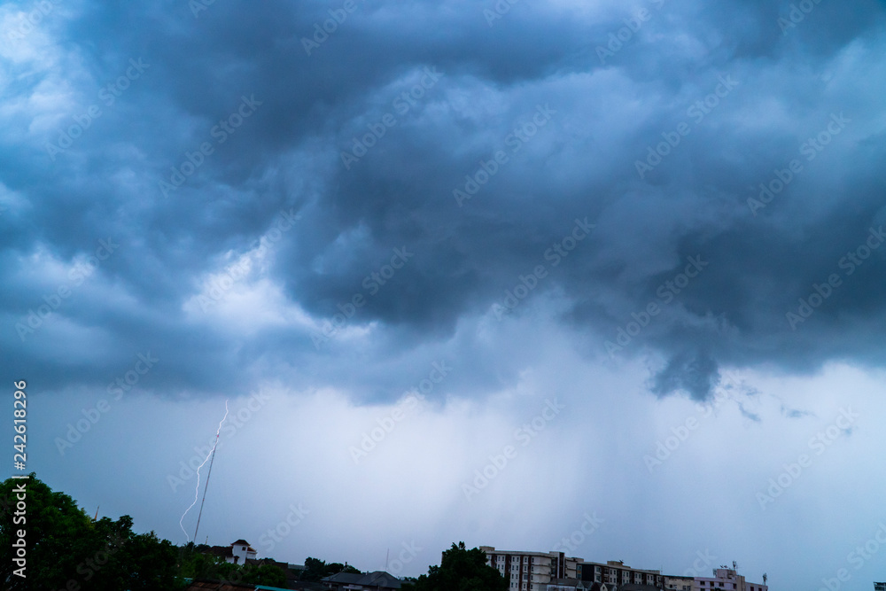 Fototapeta premium Dark clouds of a stormy sky background with part of the rain showers in the city and a powerful thunderbolt flashes down to some target on the ground.