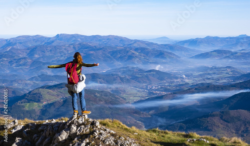 Hiker with backpack standing on top of the mountain and enjoying valley view.