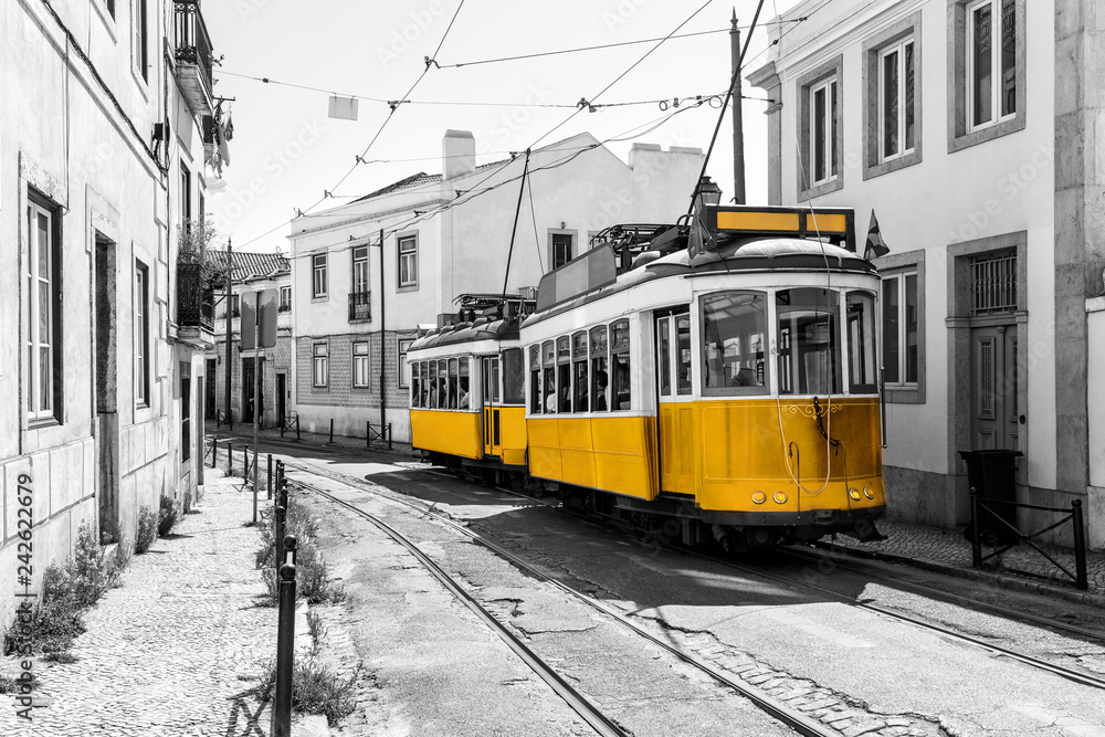 Yellow vintage trams on old streets of Lisbon, Alfama, Portugal, popular touristic attraction and destination. Black and white picture with a coloured tram.