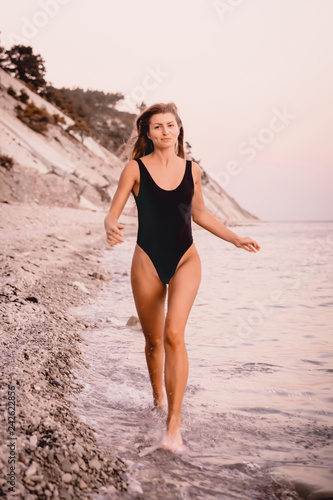 Happy blonde woman in black swimwear run and play at sea beach with warm sunset colors.