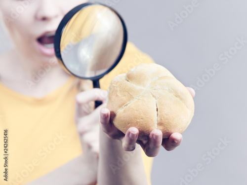 Shocked woman magnifying bun bread roll