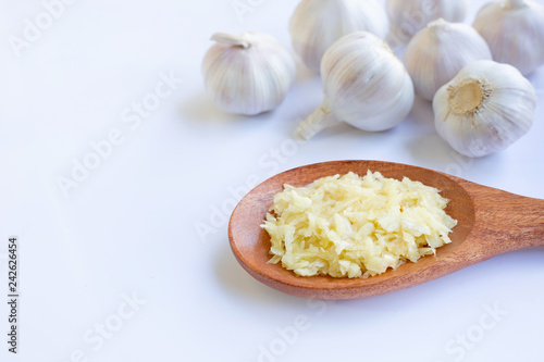 Fresh chopped garlic on wooden spoon with garlic head on white.