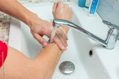A man washes his hands up to the elbows under the tap photo