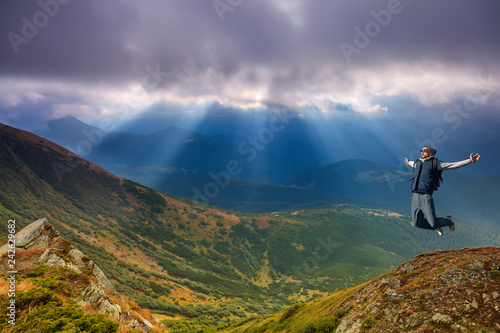 Young man jumping on top of a mountain against the sky