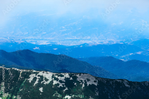 Beautiful foggy alpine high mountains peaks, blue sky background. Amazing Mountain hiking paradise landscape, summertime.