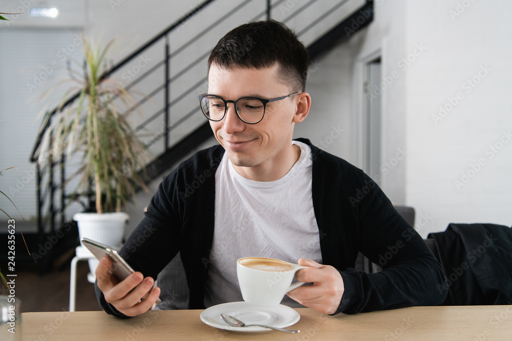 Happy young man browsing internet on smartphone sitting at outdoor cafe. Happy young man browsing internet on smartphone sitting at outdoor cafe.