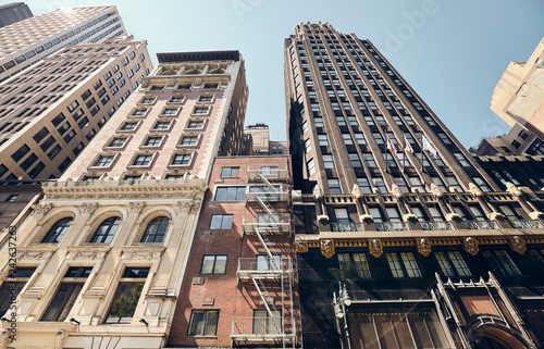 Looking up at old New York buildings, color toned picture with a lens flare, USA.