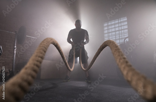 Silhouette of man working out with battle ropes at gym.