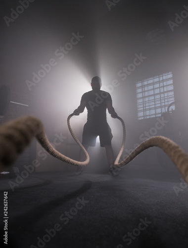 Silhouette of man working out with battle ropes at gym.