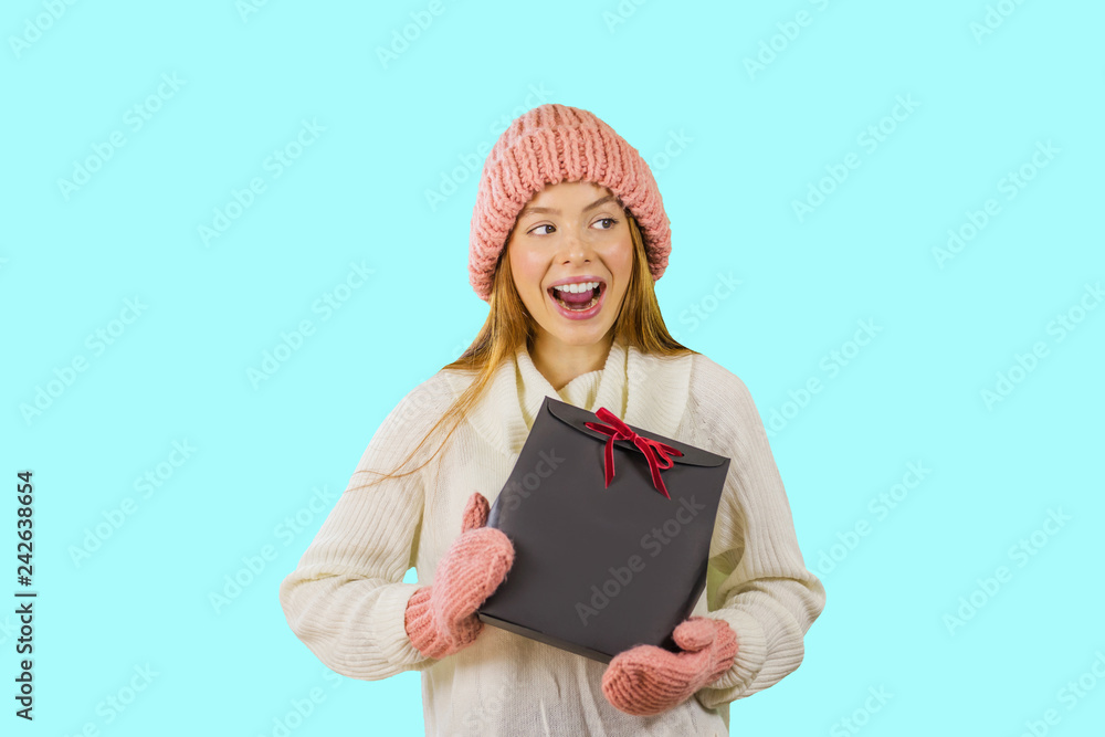 A girl with gift in her hands in warm hat and gloves looks to the side and smiles. A girl with gift in her hands in warm hat and gloves looks to the side and smiles.