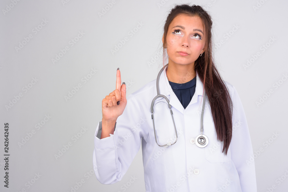 Young beautiful woman doctor thinking while pointing finger up Young beautiful woman doctor thinking while pointing finger up