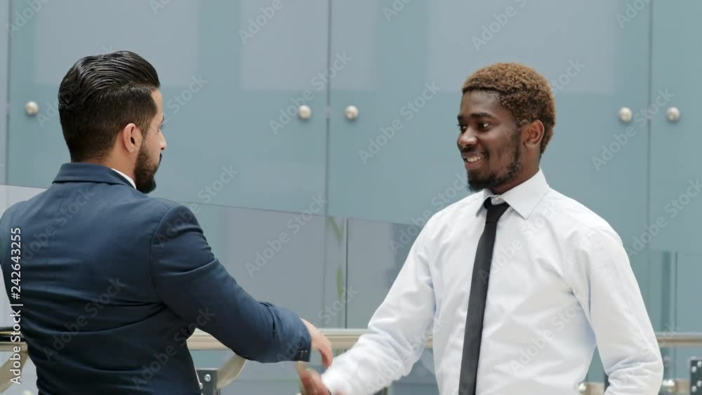 Over-the-shoulder shot of African American clerk coming closer to his Arabian coworker, shaking hands, and going out together Over-the-shoulder shot of African American clerk coming closer to his Arabian coworker, shaking hands, and going out together